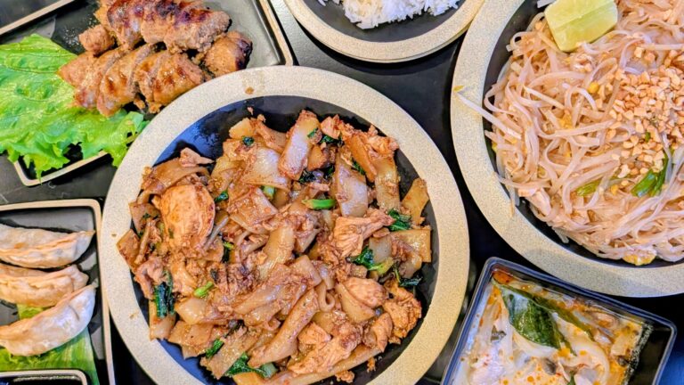 dinner table with Thai dishes including Pad See Ew, Potstickers, Pad Thai, and Tom Kha soup